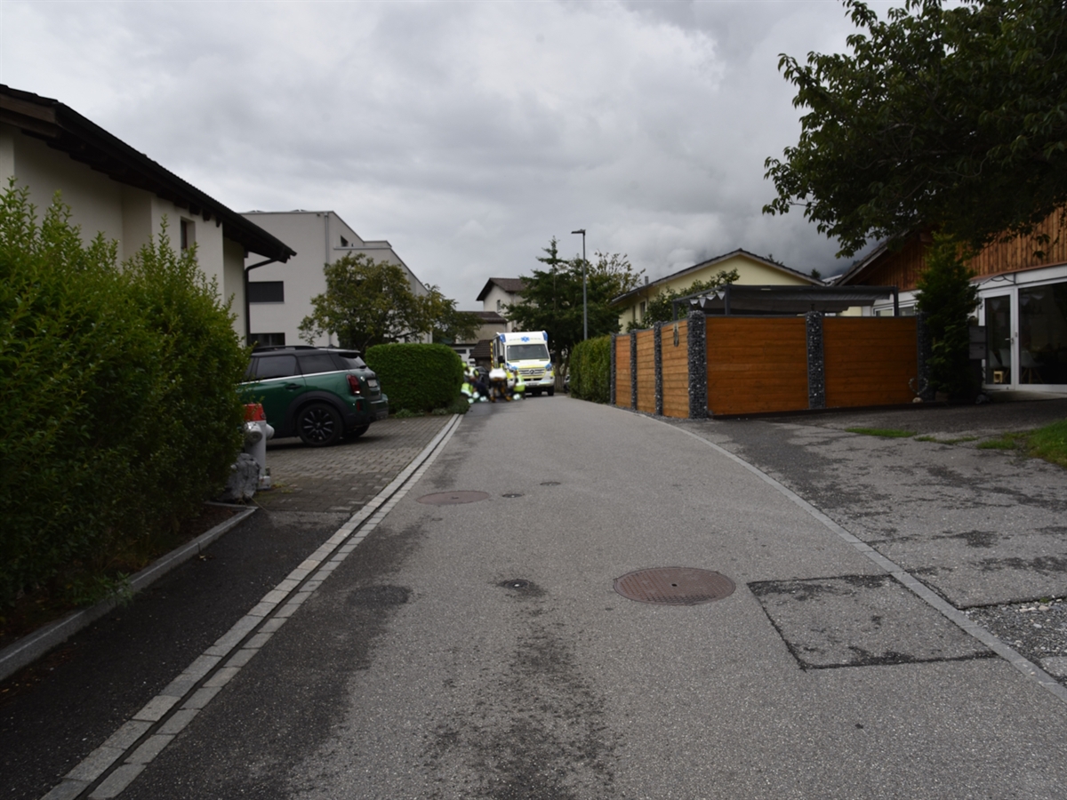 Die Unfallörtlichkeit im Quartier in Trimmis. Im Hintergrund ein Rettungsfahrzeug der Rettung Chur. Einsatzkräfte knieen am Boden und betreuen das verletzte Kind.