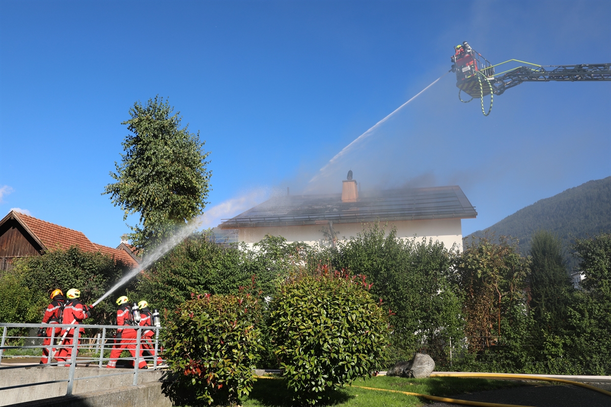 Feuerwehrleute löschen vom Boden und von der Drehleiter das rauchende Dach