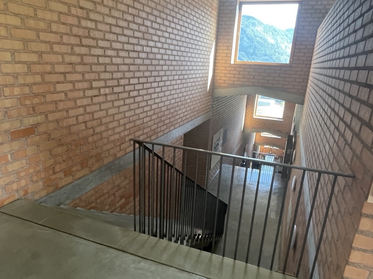 Blick in das mehrstöckige, terrassenartige Treppenhaus, in welchem der Knabe ein Stockwerk tiefer fiel. Die Wände des Treppenhauses sind mit Sichtziegelsteinen gebaut. Die Betontreppe wird durch ein Metallgeländer begrenzt.
