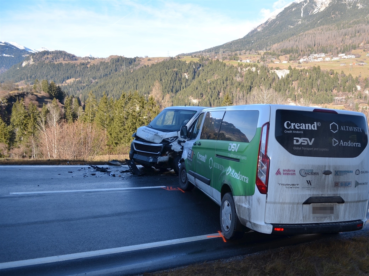 Die beiden Lieferwagen stehen einander, im Schatten, quer auf der Fahrbahn gegenüber. Die Landschaft, mit Vazerol im Hintergrund, wird durch die Sonne hell beleuchtet. Der mit Schleierwolken durchzogene blaue Himmel rundet das Bild ab.