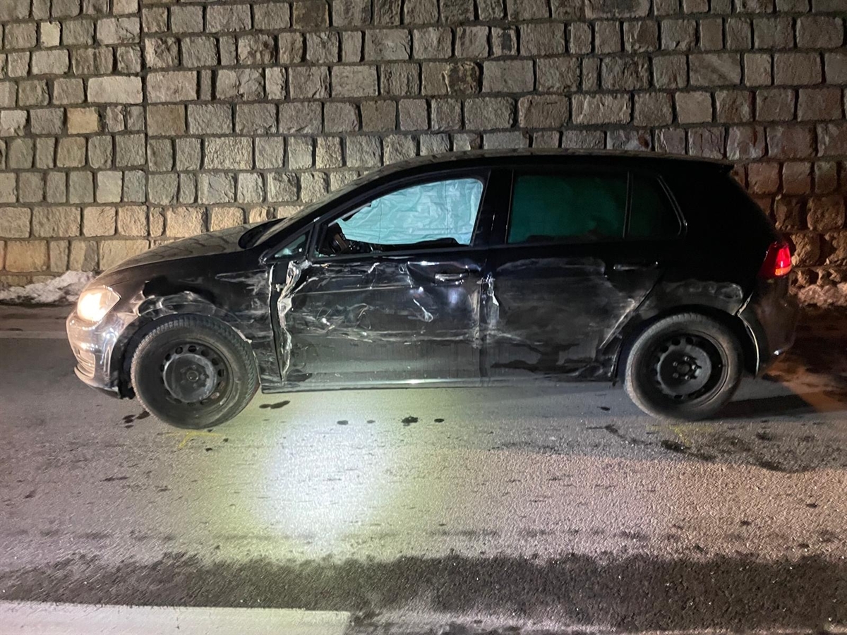 Seitliche Aufnahme eines dunklen Autos mit beschädigter Fahrerseite auf der ganzen Länge. Die Seitenairbags sind ausgelöst.