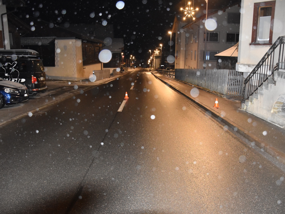 Der Strassenverlauf wird links und rechts von Häusern begrenzt. Zwei Kegel markieren die Kollisionsstelle. Schneeflocken werden in der Nacht durch den Fotoblitz aufgehellt und sichtbar gemacht.