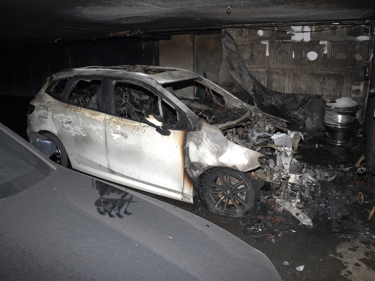 Das ausgebrannte Hybrid-Auto in der verrussten Tiefgarage. Neben dem Auto steht ein weiteres, mit Russ überdecktes Auto. Im Hintergrund verbranntes Material, welches in der Garage deponiert war.