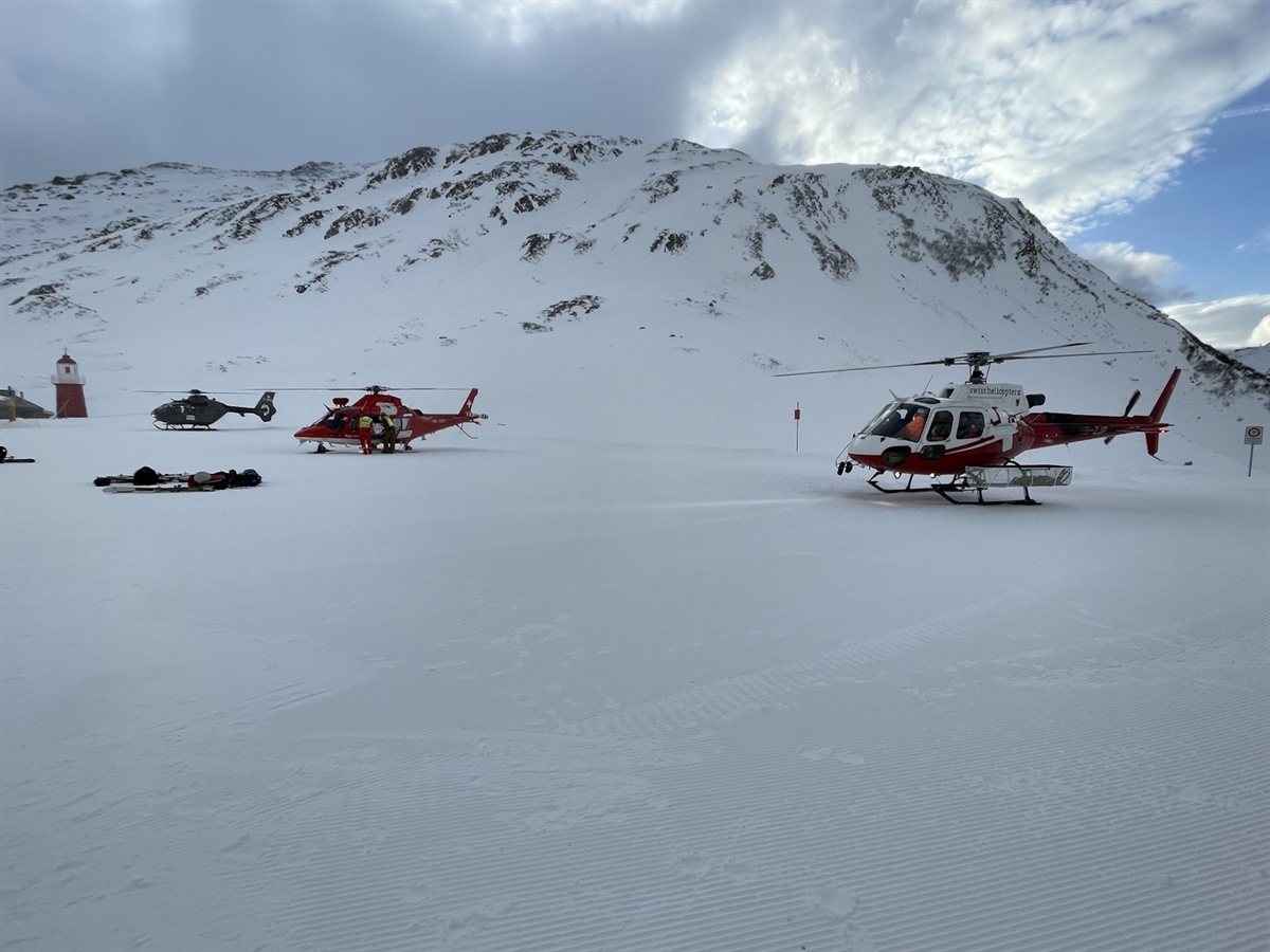 Drei Helikopter auf dem Oberalppass. Im Hintergrund grenzen Berge den teilweise bedeckten Horizont ab.