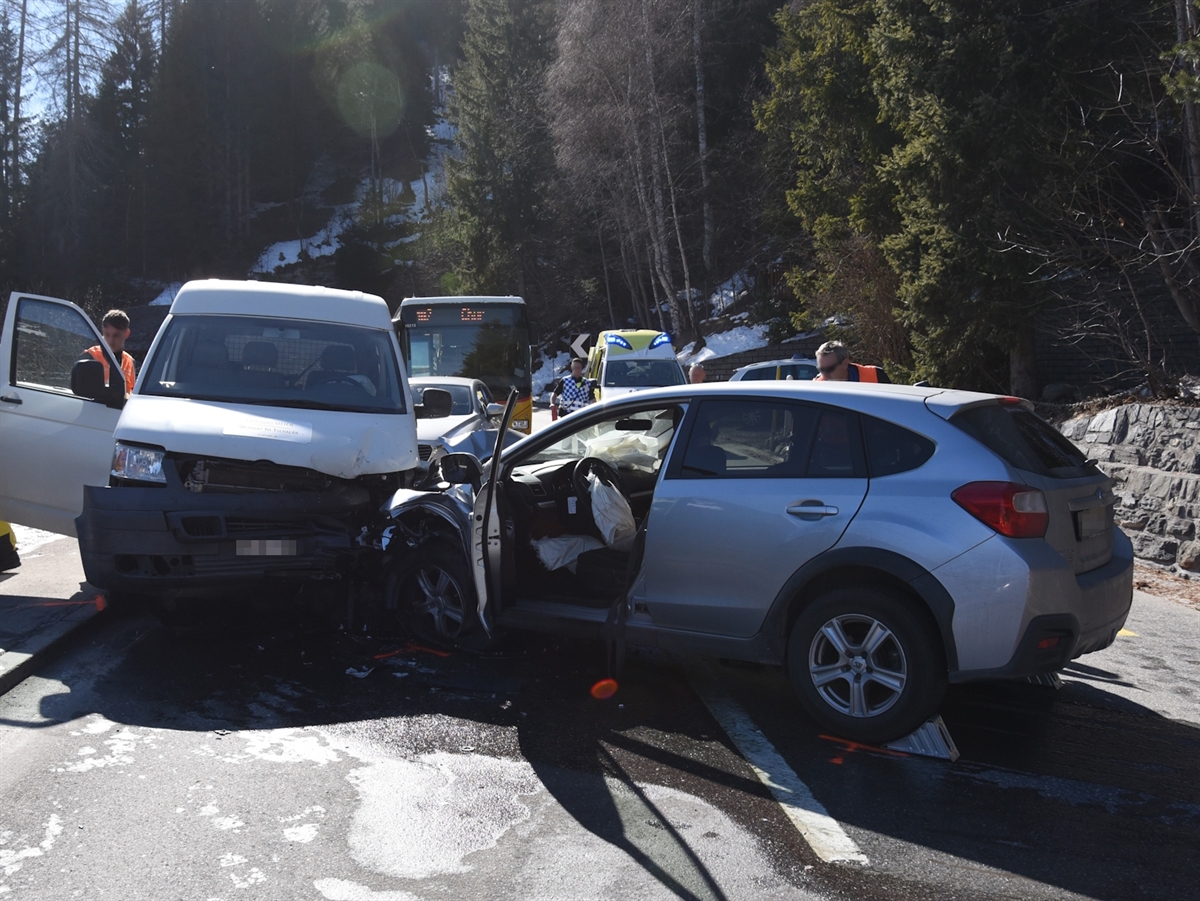 Links das entgegenkommende Fahrzeug und rechts das Auto des Seniors. Im Hintergrund die Silhouetten eines Postautos, eines Rettungswagens sowie eines Polizeifahrzeuges. Zwei Polizisten begutachten die Unfallstelle.