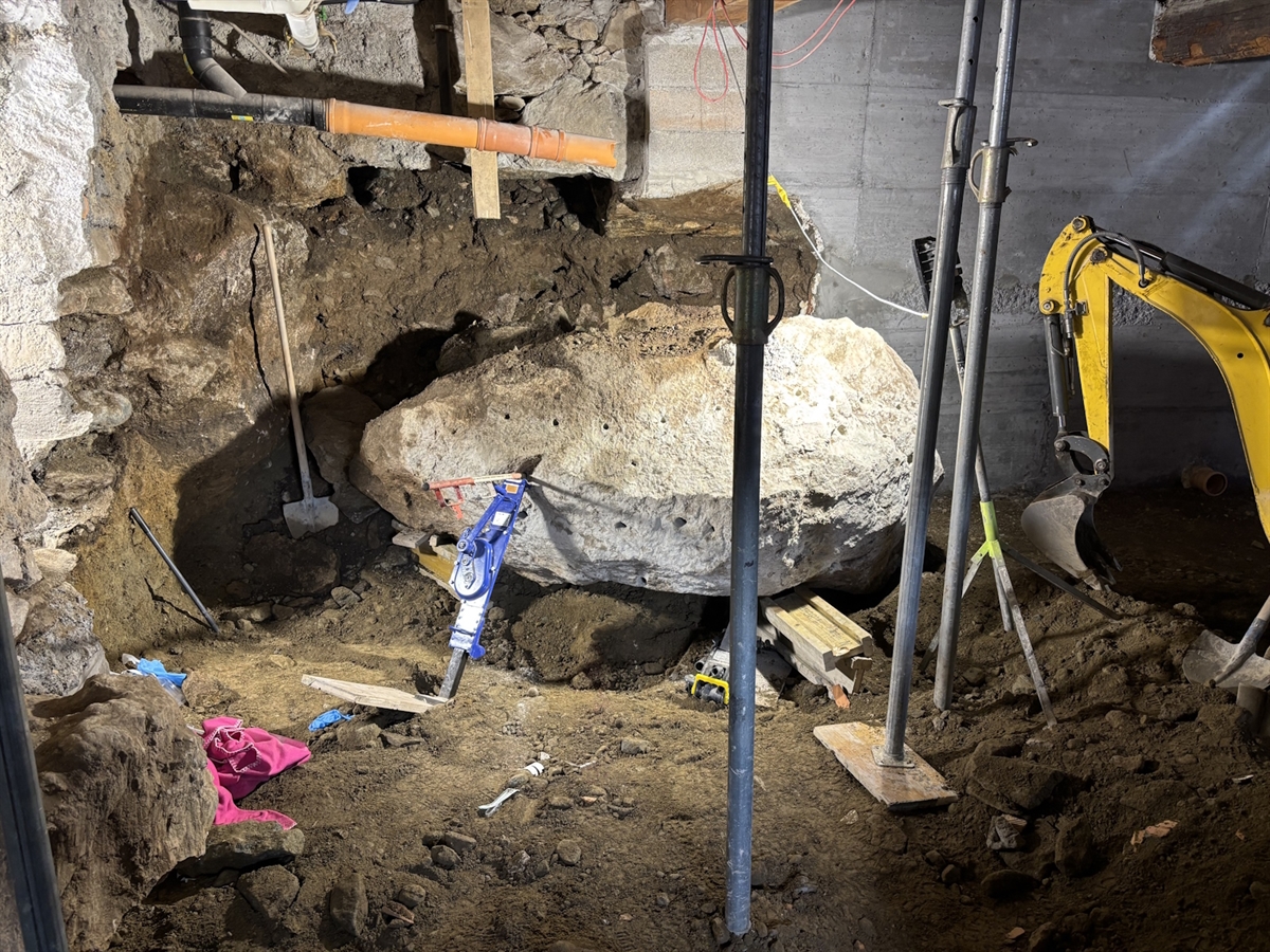 Der aus der Mauer gekippte Stein liegt auf dem Erdboden im Keller. Stützen zwischen Boden und Decke sowie solche, die den Stein stabilisieren.