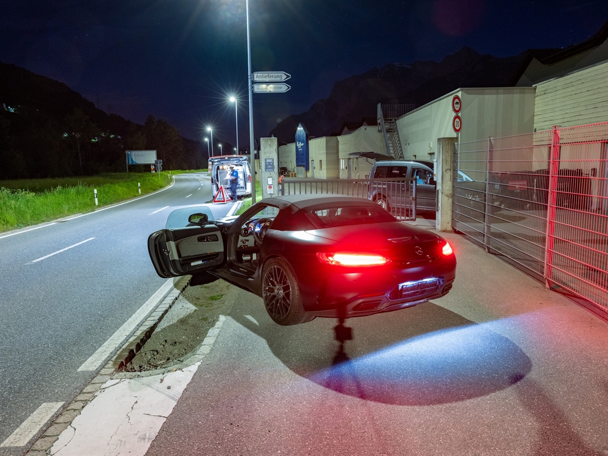 Nachtaufnahme. Ein Sportwagen mit offener Fahrertüre. Im Hintergrund ein Polizeiauto, ein Faltsignal mit den Aufschriften 