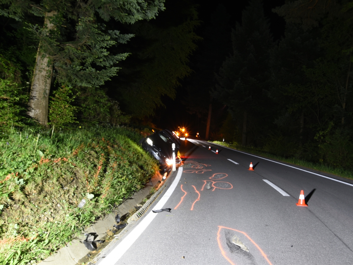 Die nächtliche Unfallstelle mit dem Strassenverlauf in Richtung Pass. Auf der Fahrbahn sind verschiedene Schleuder- und Kratzspuren mit Spray markiert. Das Unfallauto liegt an der Böschung angelehnt in der Rinne links von der Fahrbahn.
