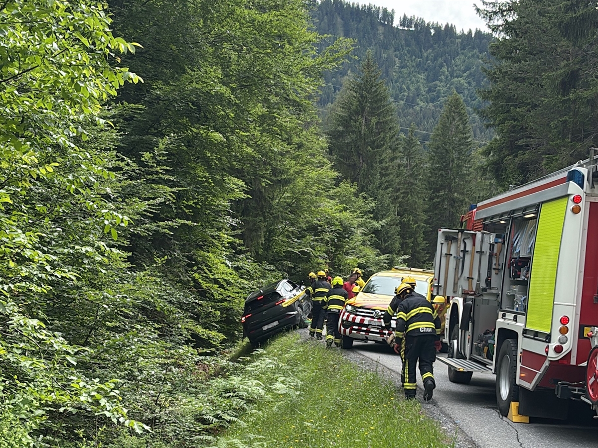 Einsatzfahrzeuge der Strassenrettung und eines Abschleppdienstes. Daneben in Schräglage zwischen Strasse und Abhang ein Personenwagen.