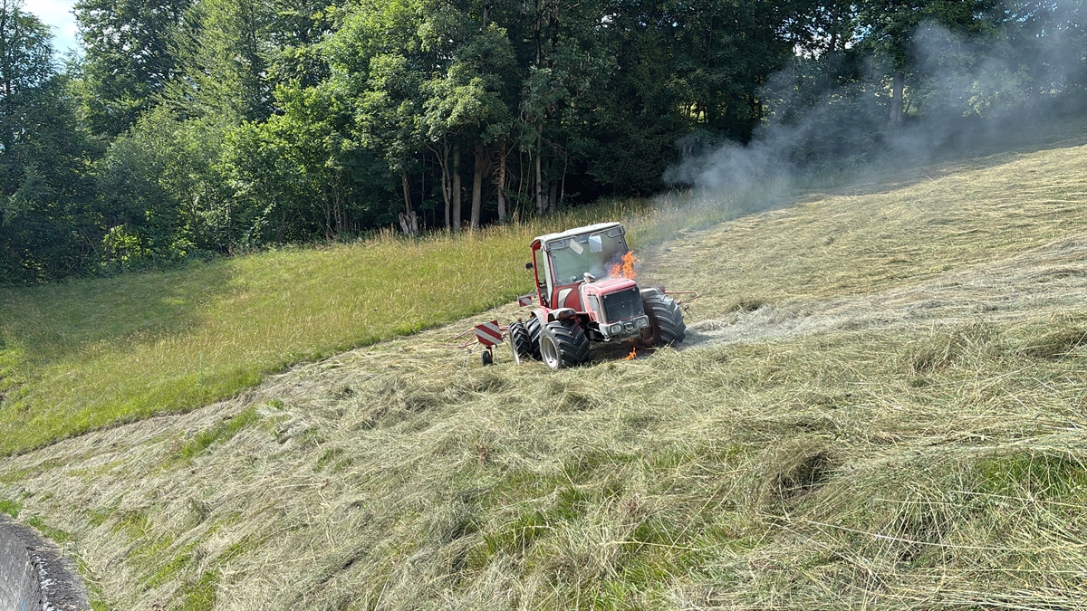 Das landwirtschaftliche Fahrzeug in der gemähten Wiese. Feuer tritt aus der Motorhaube aus.