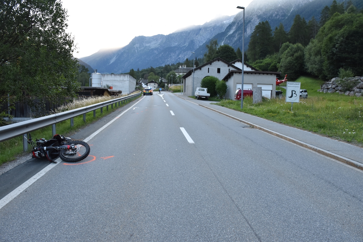 Die Strada Principale, links im Bild liegt das Motorrad am Strassenrand. Im Hintergrund Häuser.