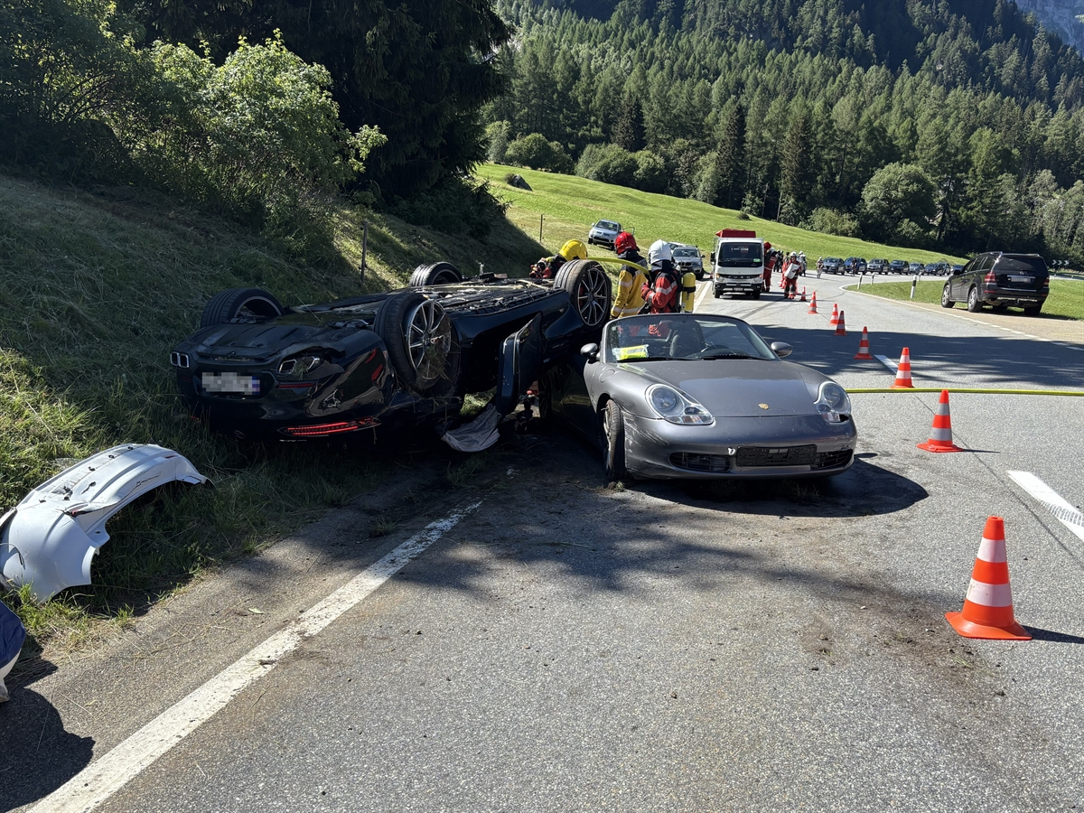 Die beiden Autos mit Totalschaden. Das eine Fahrzeug liegt auf dem Dach, zu einem Teil an der Böschung, zum anderen auf dem zweiten Auto. Hinter ihnen die Strassenrettung, vor ihnen ein Autoteil des dritten Autos.