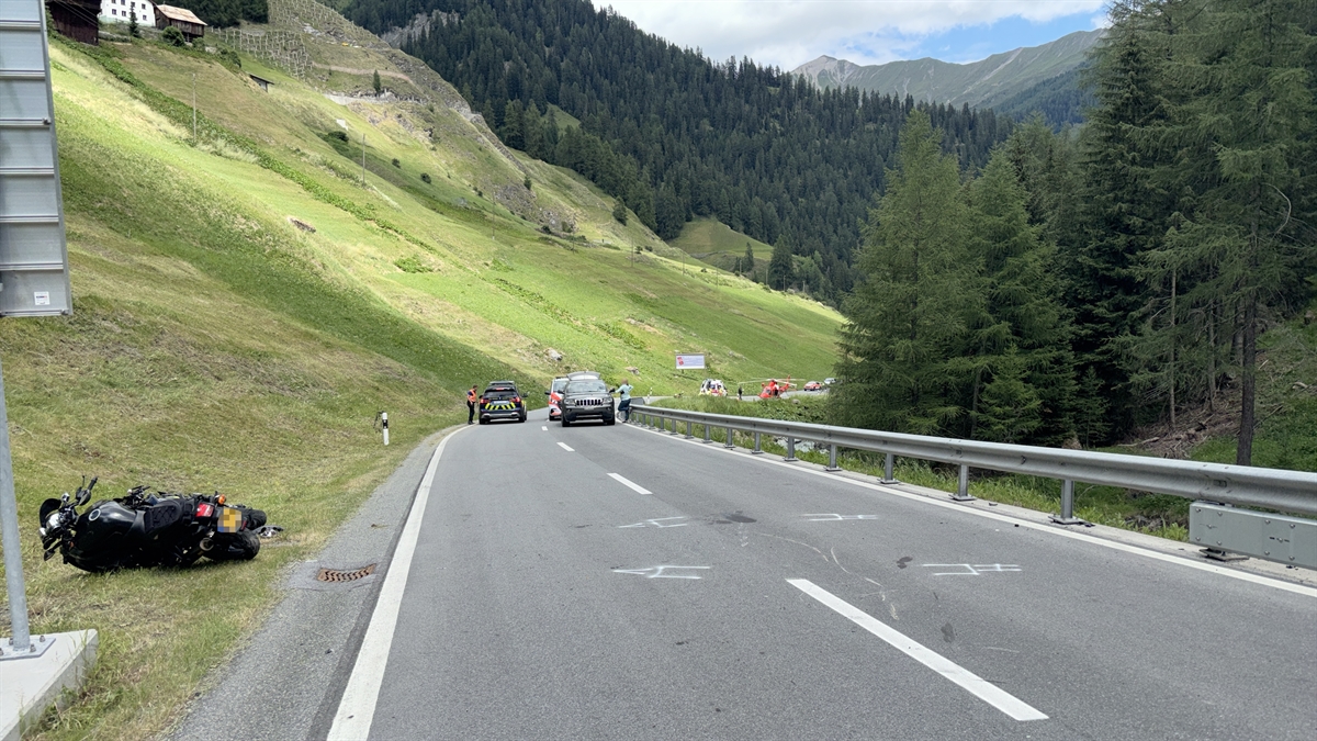 Die Strasse, neben welcher einer der verunfallten Motorräder liegt. Im Hintergrund ein Fahrzeug, des BAZG, ein Privatfahrzeug und ein Auto der Kantonspolizei Graubünden.