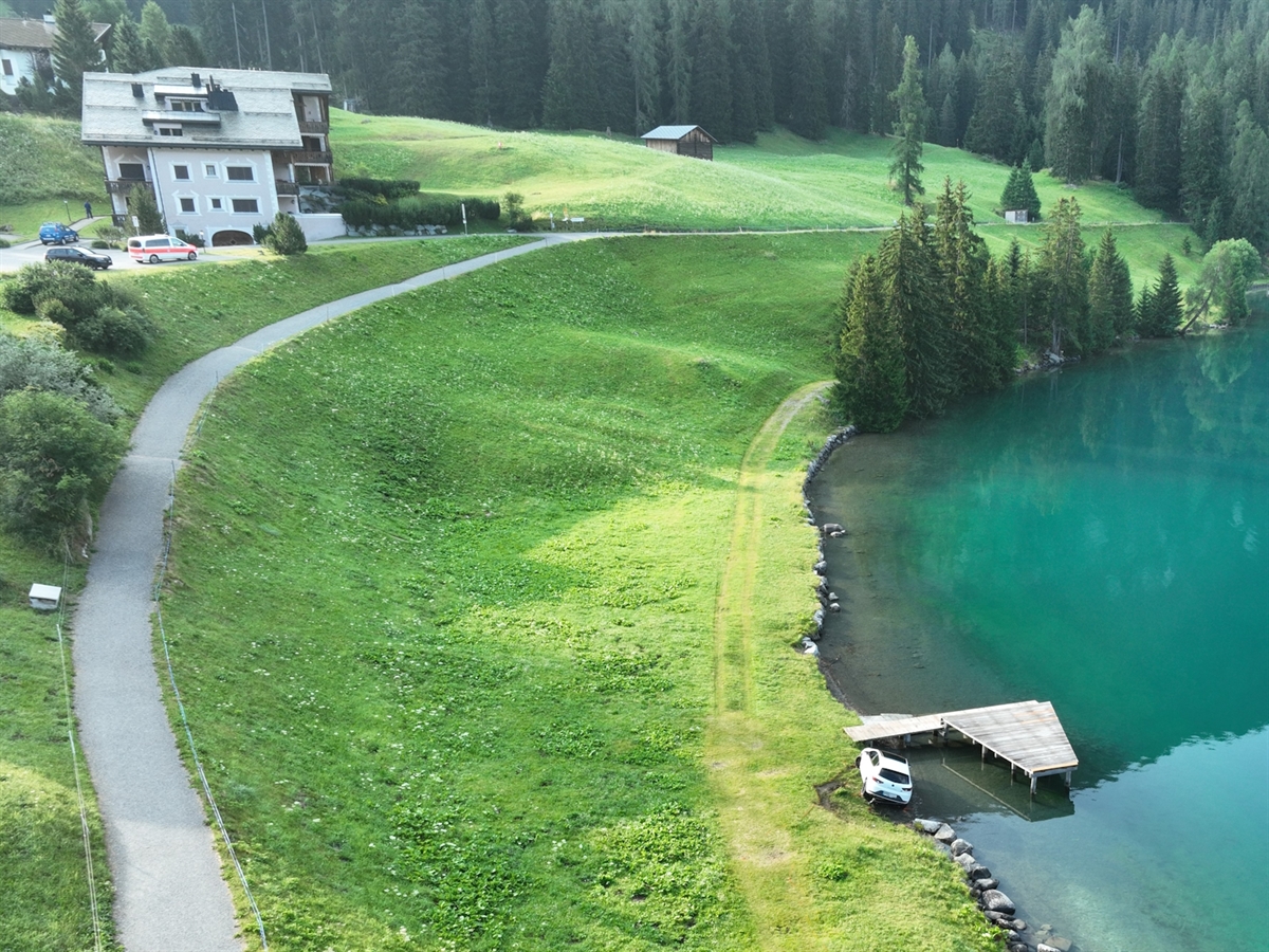 Rechts der Davosersee und links davon Wiesland. Am Seeufer das Auto.