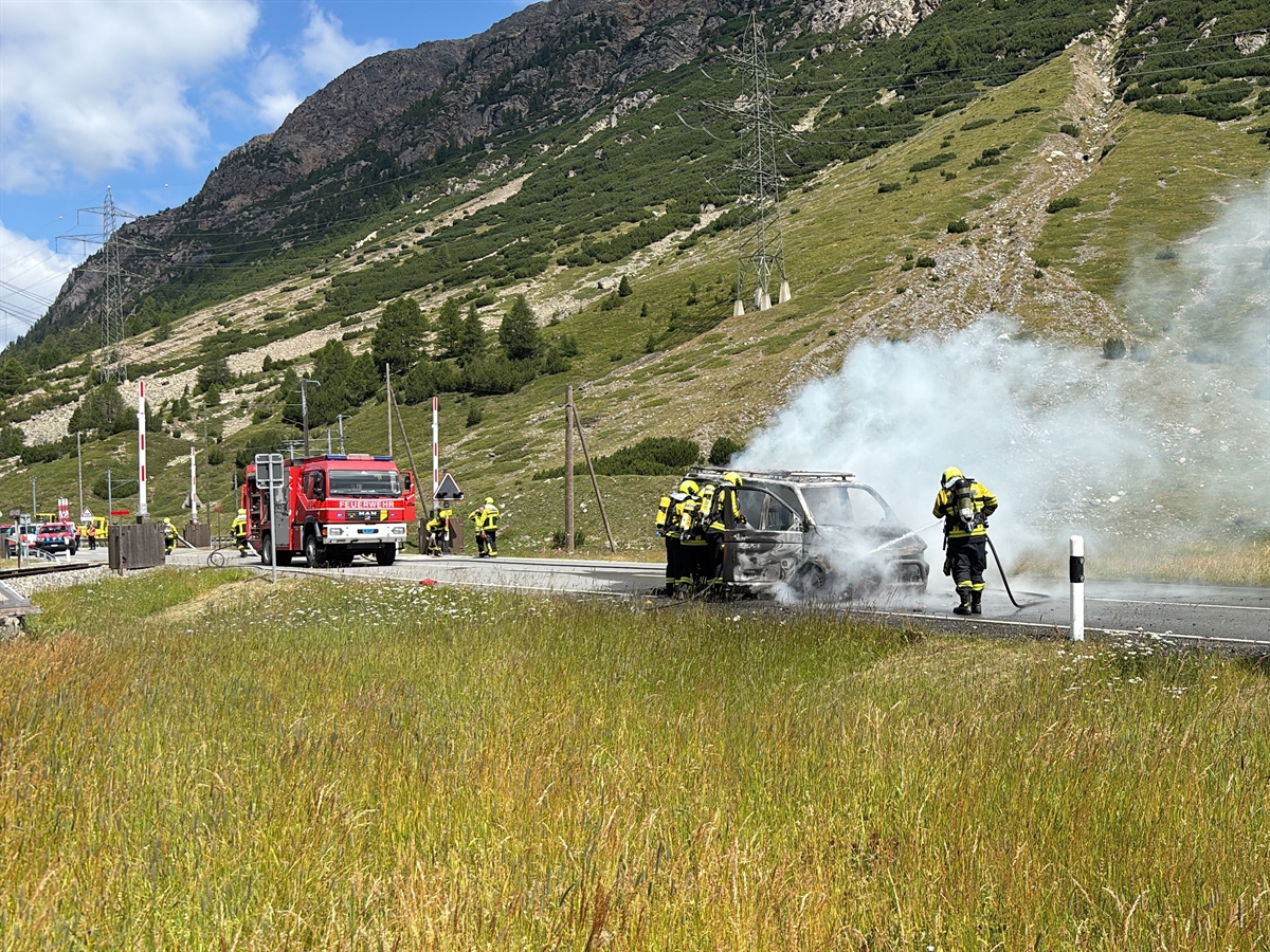 Das ausgebrannte Fahrzeug, rundherum Feuerwehrleute bei den Löscharbeiten. Im Hintergrund das Feuerwehrauto.
