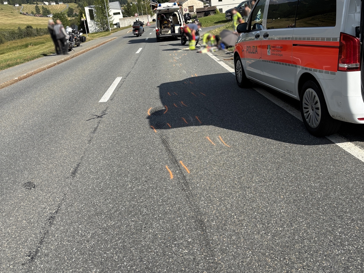 Auf der Fahrbahn sind Bremsspuren eingezeichnet. Rechts steht ein Polizeifahrzeug. Im Hintergrund versorgen Rettungsleute den verletzten Motorradfahrer.