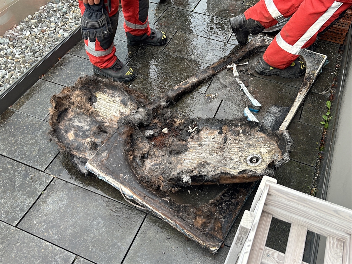 Die geschmolzenen Überreste der Kunststoffbadewanne. Zwei Feuerwehrleute begutachten das Brandobjekt.