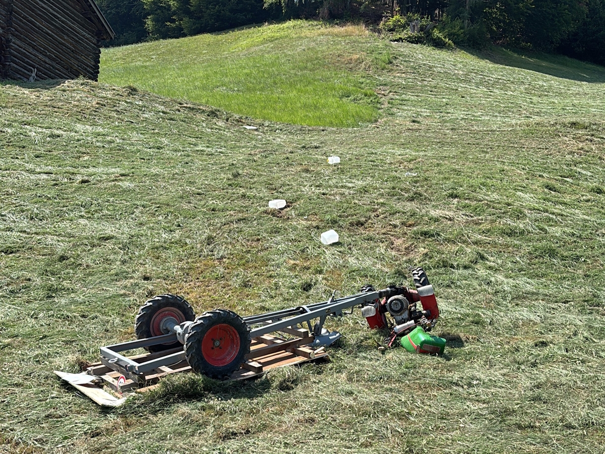 Der Motoreinachser liegt seitlich auf einer gemähten Wiese. Im Hintergrund ein Stall sowie Wald.