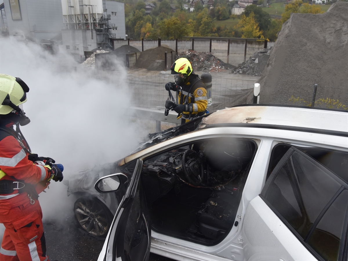 Zwei Feuerwehrleute bekämpfen den Fahrzeugbrand auf der A13. Im Hintergrund ein Gebäude des Kieswerks Maienfeld neben der A13.