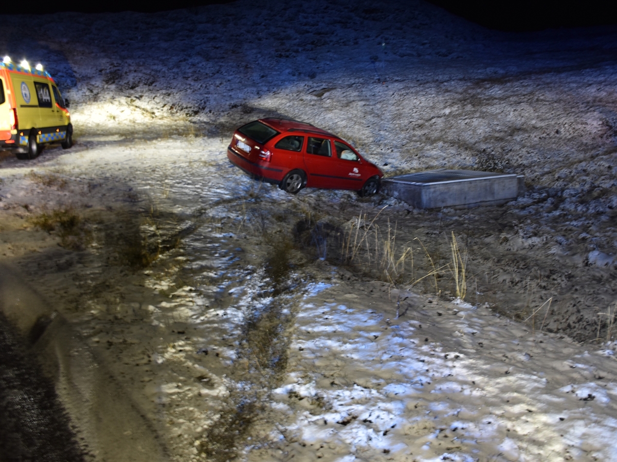 Das Auto steht auf der schneebedeckten Wiese neben der Oberalpstrasse, mit der Front zum Schacht. Am linken Bildrand ist die Seite eines Rettungswagens erkennbar. Das Blaulicht der Einsatzfahrzeuge erhellt die Morgendämmerung.