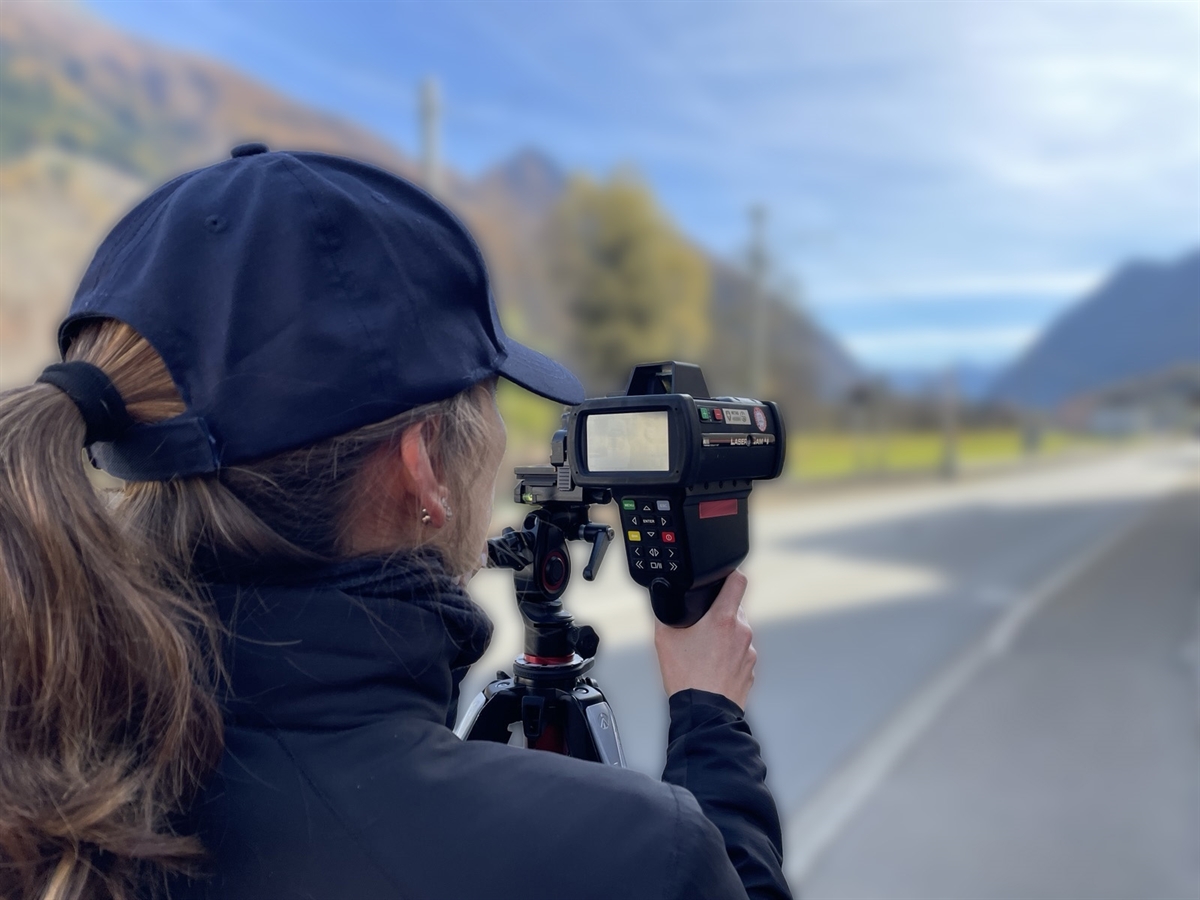 Unscharfer Hintergrund. Im Fokus eine Polizistin mit einem Lasermessgerät. 