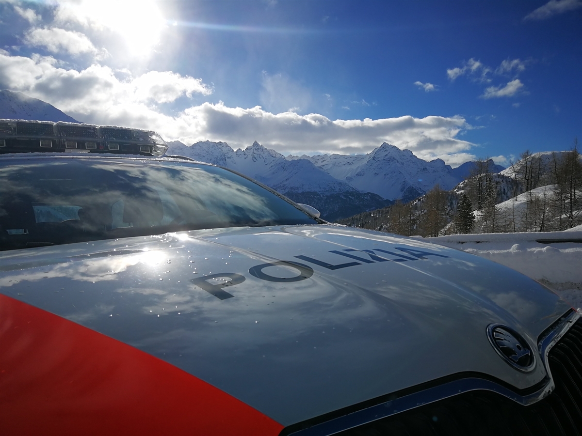 Ein Polizeiauto in sonniger und winterlicher Berglandschaft.