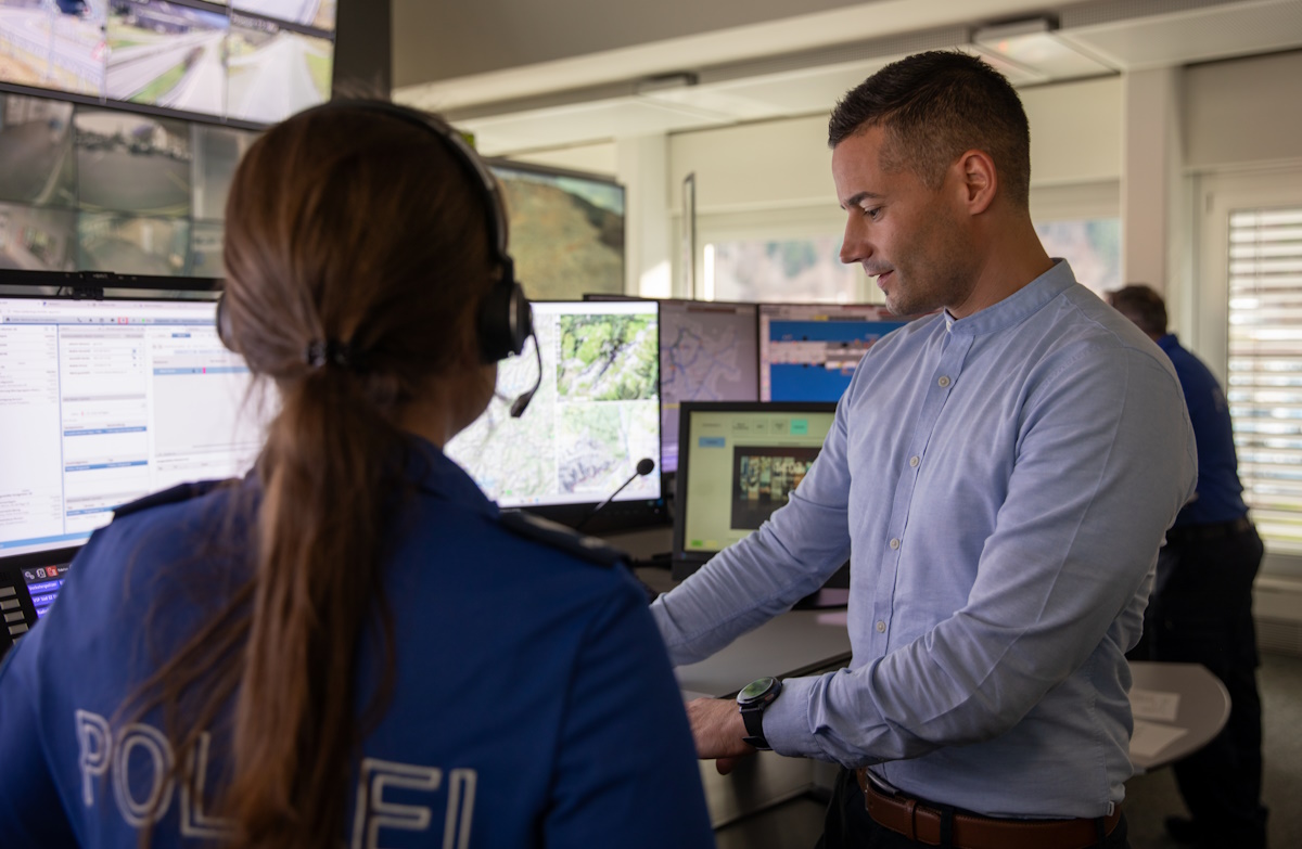 Peter Blatter vor den Bildschirmen der Einsatzleitzentrale im Gespräch mit einer Mitarbeiterin