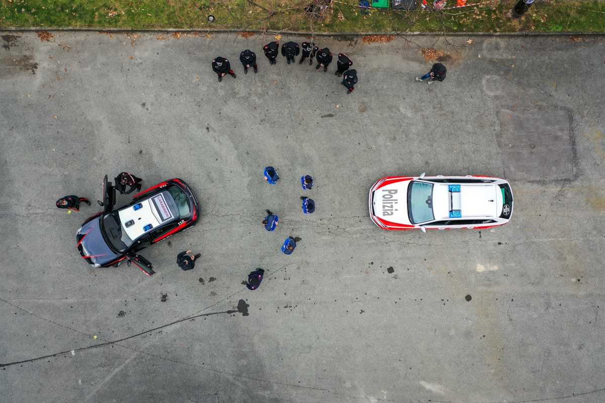 Luftaufnahme auf ein Fahrzeug der Carabinieri und eines der Polizei. Um die Fahrzeuge stehen formierte Einsatzkräfte.