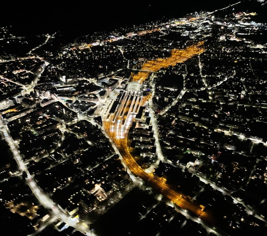 Nachtbild der Stadt Chur aus dem Helikopter. Schön beleuchteter Bahnhof von Chur mitten in der Stadt.