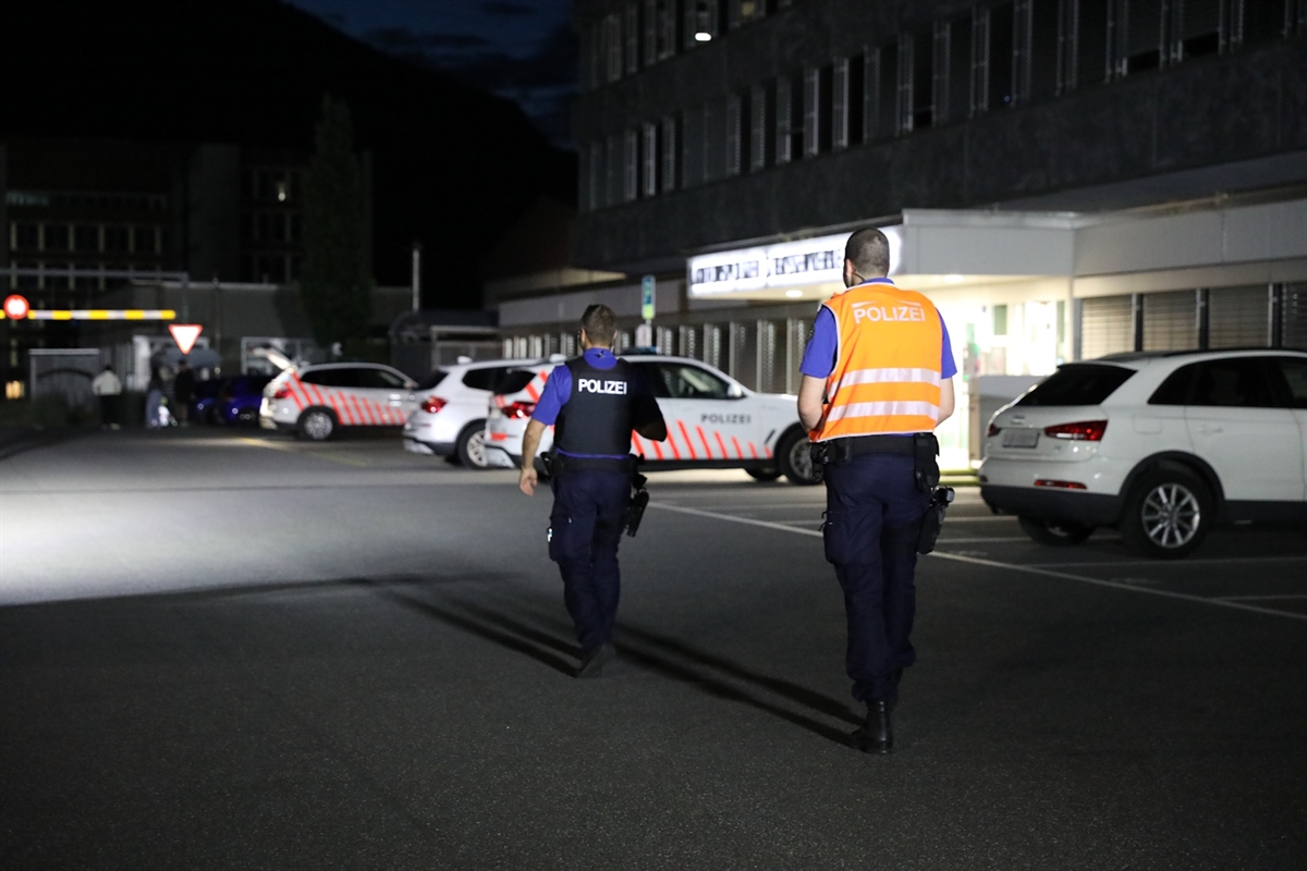 Aufname im Dunkeln vor dem Polizeikommando. Zwei Polizisten laufen über den Platz in Richtung zweier Patrouillenfahrzeuge.