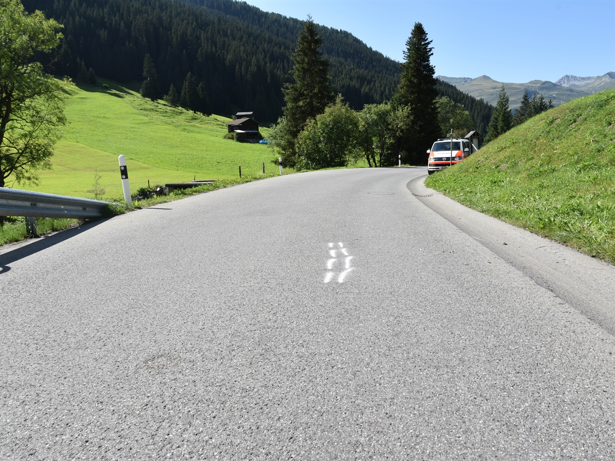 Die Fahrbahn kurz vor der Rechtskurve auf der Sertigstrasse in Davos. Eine Fahrrad-Bremsspur ist auf der Fahrbahn eingezeichnet.