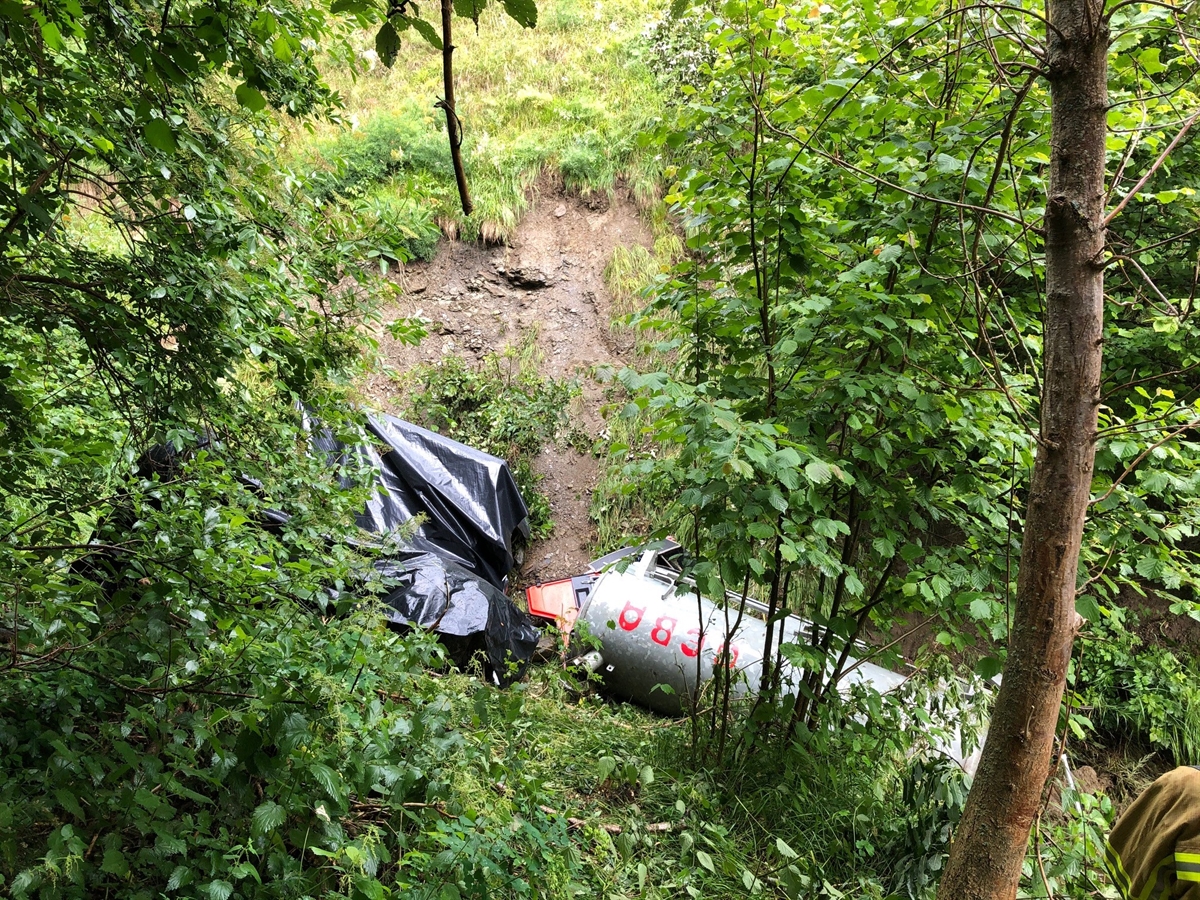 Blick aus der Böschung auf das total beschädigte Fahrzeug in Endlage. Die Führerkabine ist mit schwarzer Plastikfolie abgedeckt. Insbesondere sichtbar ist das Güllefass.