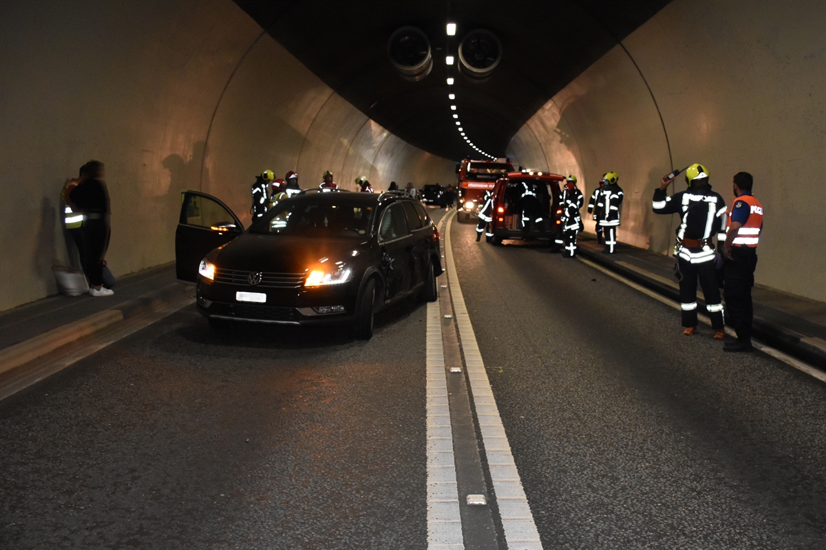 Das an beiden linken Radaufhängungen sowie der ganzen linken Seite stark beschädigte Auto im Tunnel. Weitere Personen wie Rettungskräfte und weitere Fahrzeuge sichtbar.