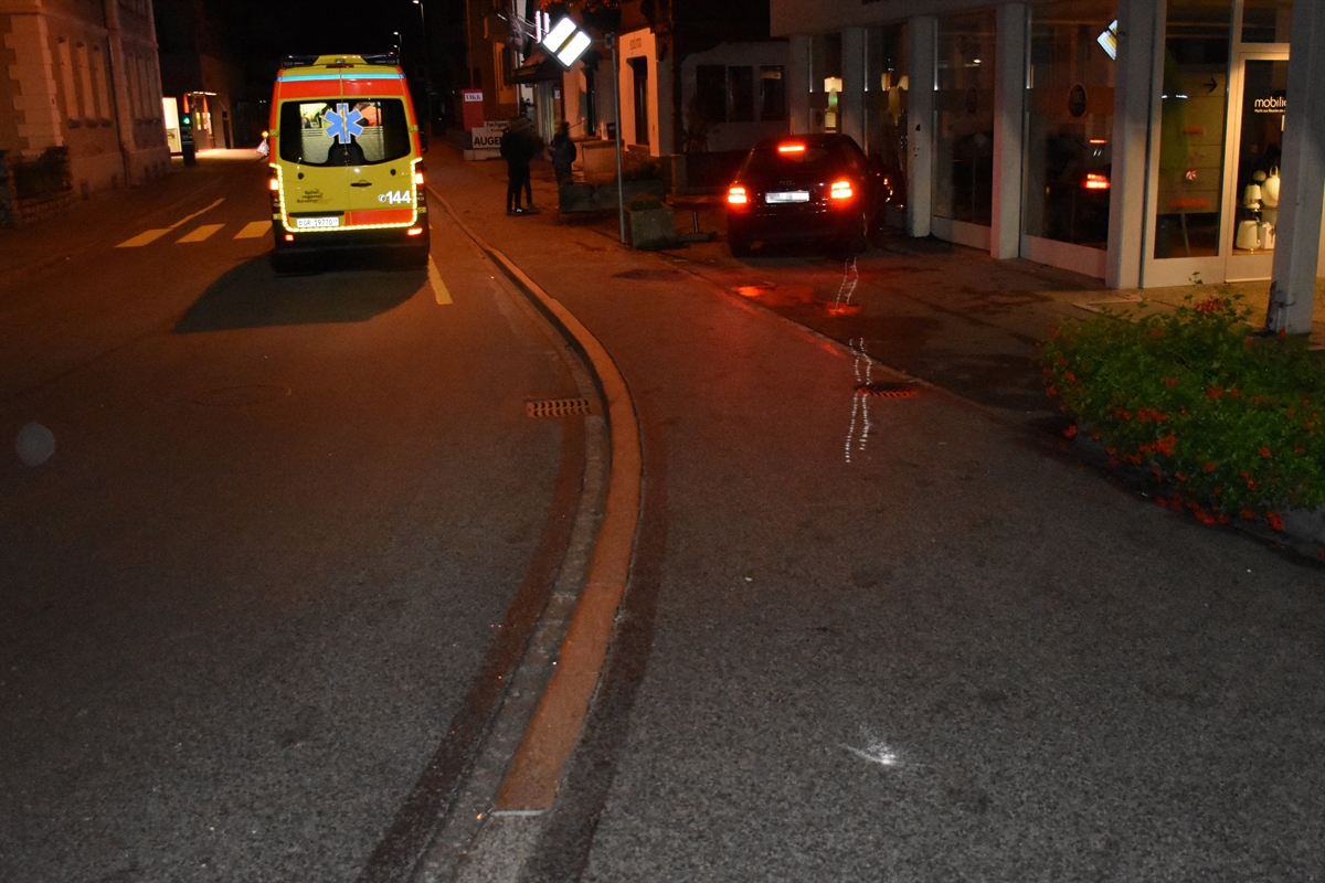 Nachtaufnahme aus der Linkskurve. Auf der Strasse eine Ambulanz, rechts davon das Trottoir. Weiter rechts das mit dem Geschäftshaus kollidierte Auto.
