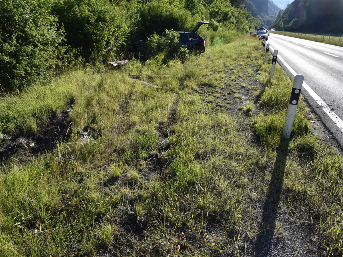 Am rechten Bildrand verläuft die Nationalstrasse N29. Links neben der Fahrbahn ragt das Heck des Unfallfahrzeuges aus dem Unterholz. Gut sichtbar ist noch die umgefahrene Signaltafel.