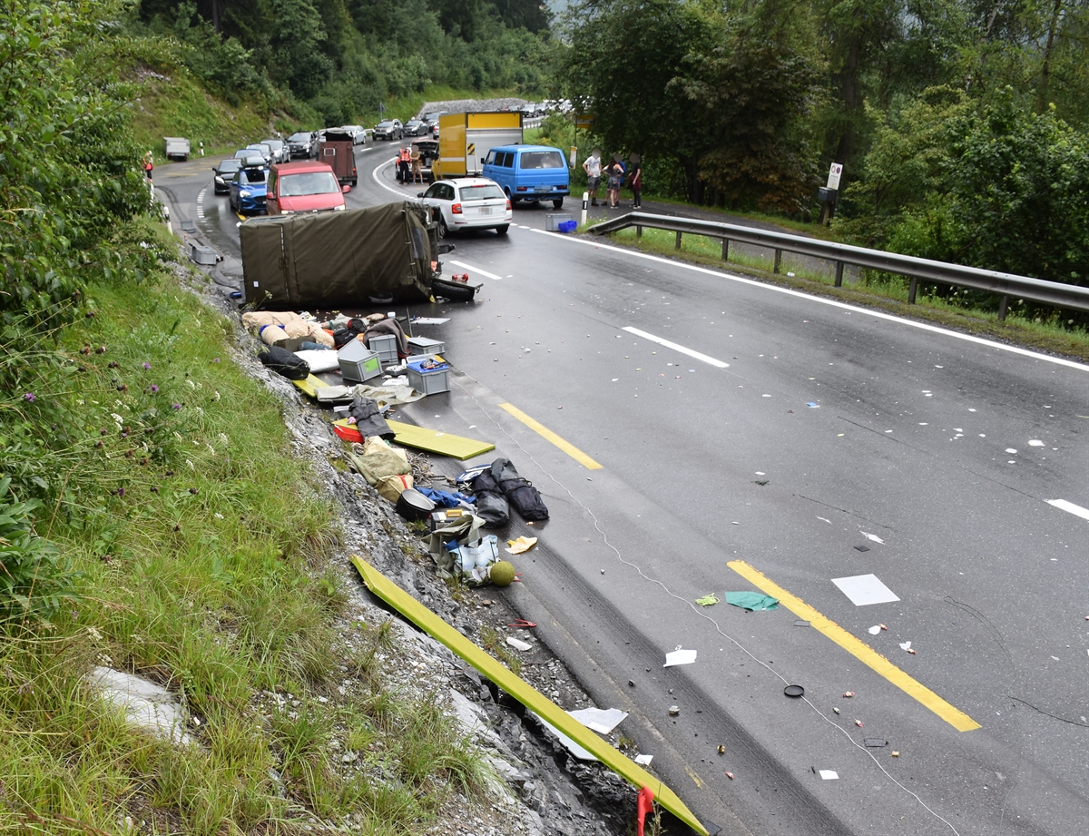 Oberalpstrasse talwärts von Flims in Richtung Trin. Im Vordergrund links liegt Reisematerial auf der Strasse, dahinter der umgekippte Lieferwagen. Im Hintergrund wartende Fahrzeuge im Rückstau.