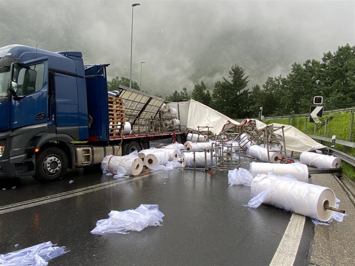 Das Sattelmotorfahrzeug steht in der Rechtskurve. Rechts neben dem Fahrzeug ist die Fahrbahn der A13 mit Plastikrollen übersäht. Die Plane mit dem gesamten Aufbau des Stattelanhängers ist runtergerissen und liegt ebenfalls auf der Fahrbahn.