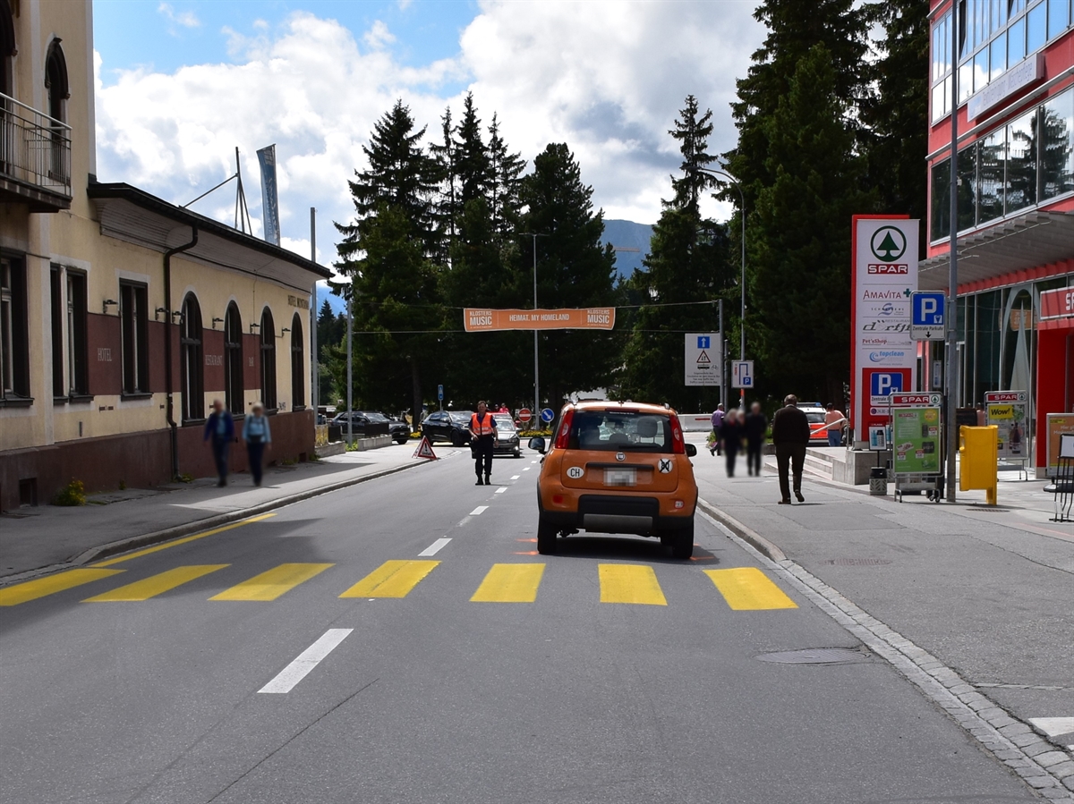 Bahnhofstrasse in Richtung Dorfinnern gesehen. Fussgängerstreifen quer über die Fahrbahn. Unmittelbar dahinter steht das Auto, welches den Fussgänger angefahren hat. Ein Polizist hält den Verkehr auf der Dorfstrasse an.