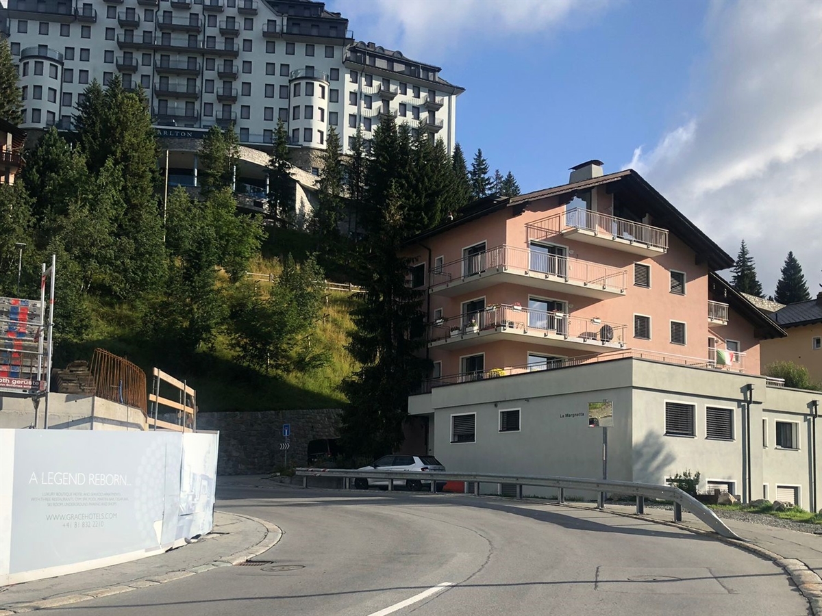 Linkskurve mit Häusern im Hintergrund und blauem Engadinerhimmel