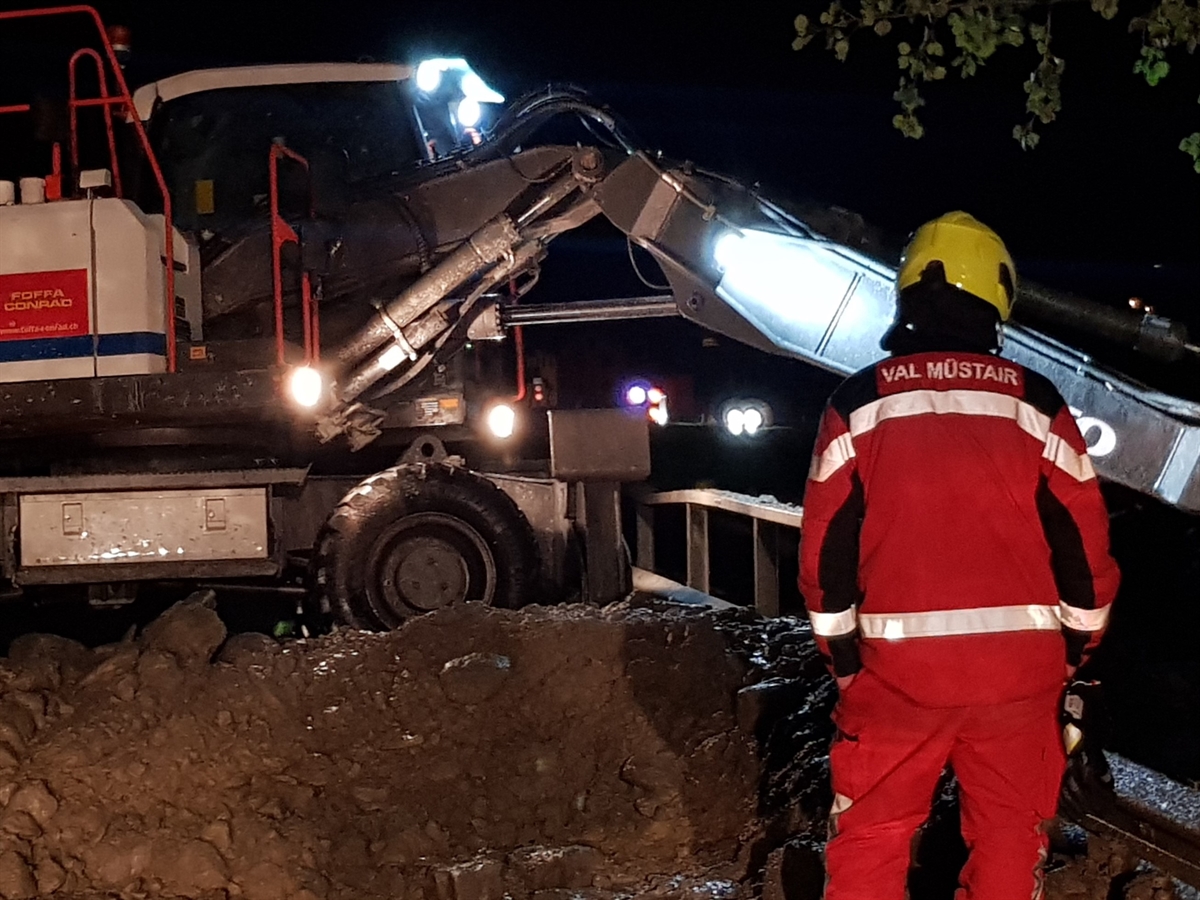 Ein Bagger im Einsatz, rechts davon ein Feuerwehrmann.