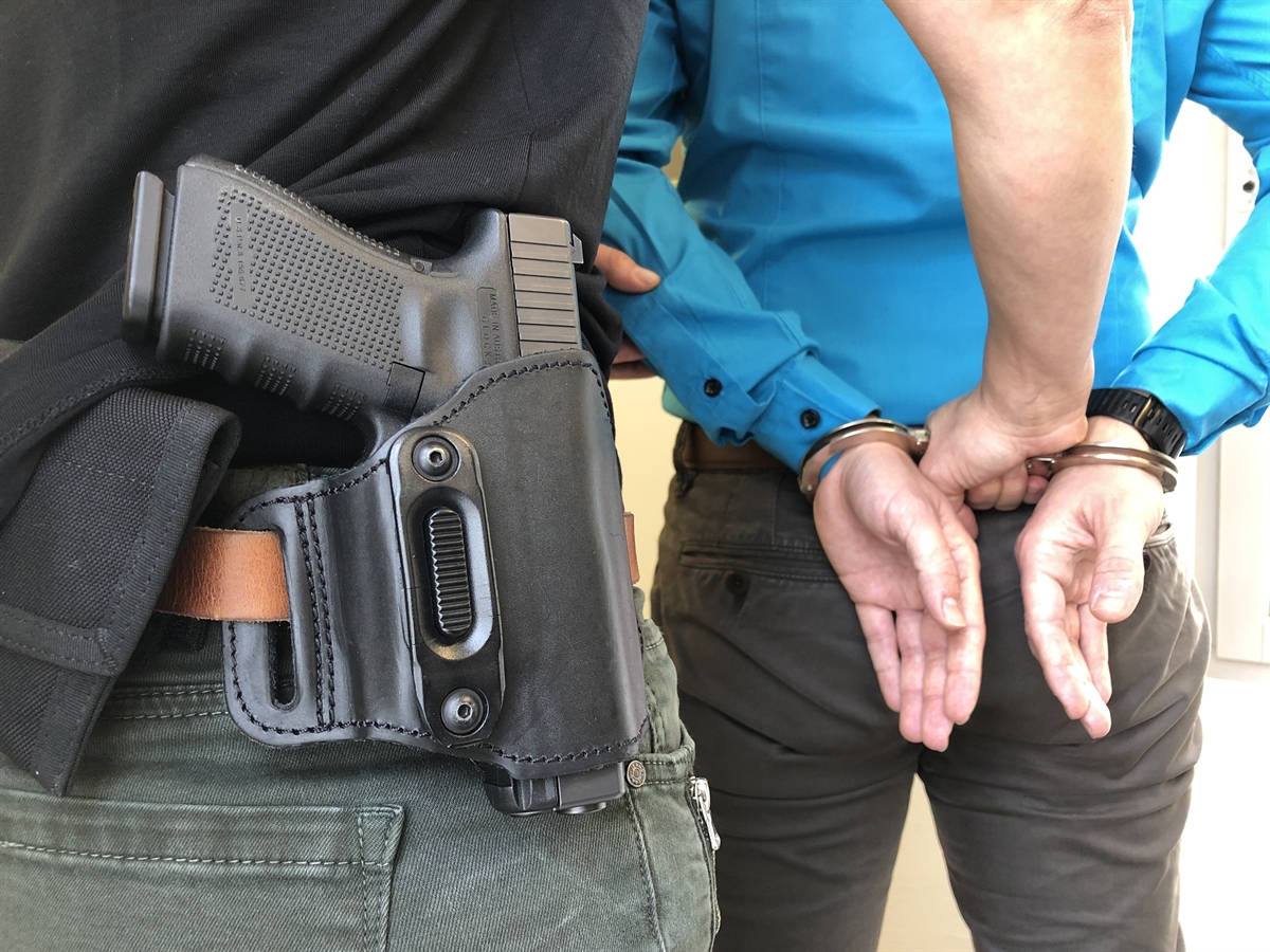 Polizist mit Pistole legt einem Mann Handschellen an