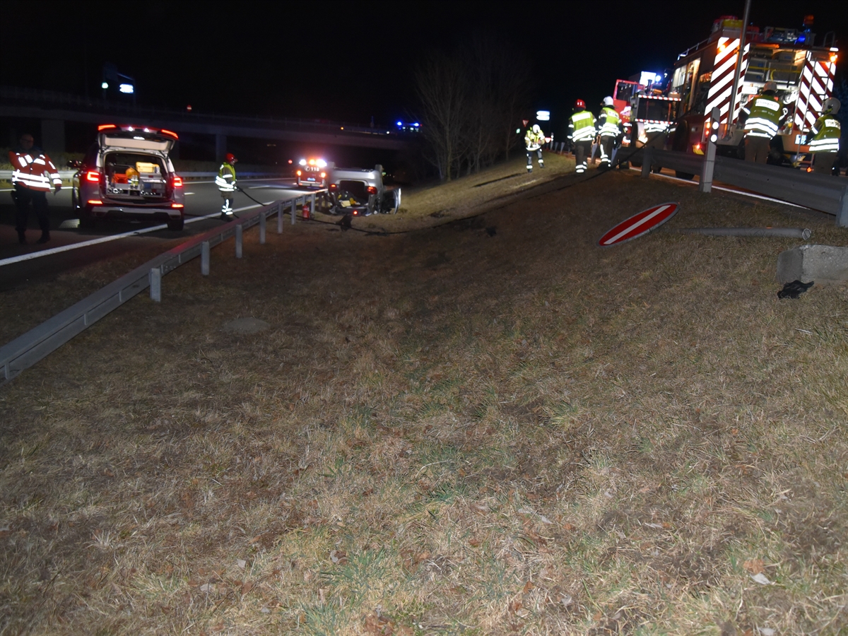 Links die Fahrspuren der Autobahn, rechts davon das Wiesenstück und weiter rechts die ansteigende Ausfahrtsrampe. Links Einsatzkräfte von Polizei und Feuerwehr, rechts solche der Feuerwehr und mittig das Auto auf dem Dach.