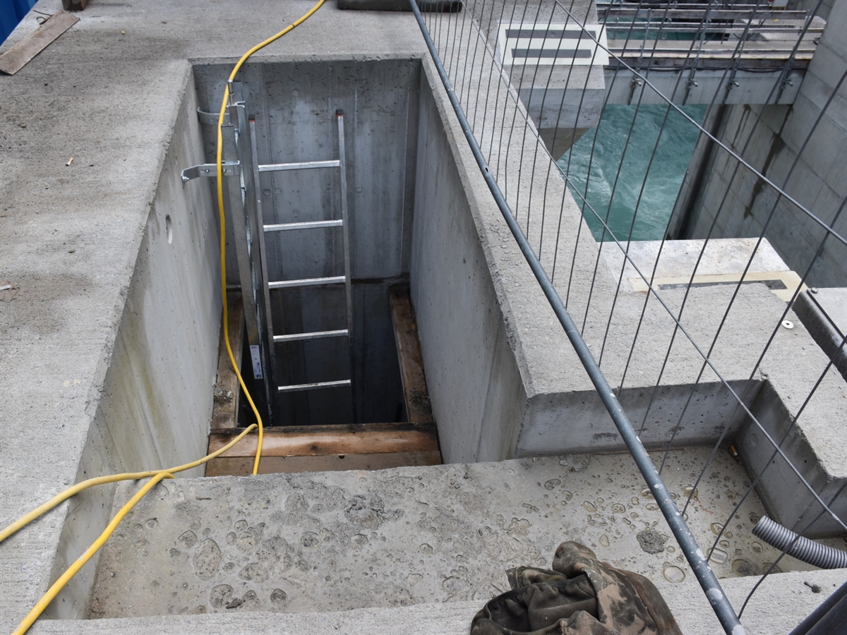 Aus dem Schacht führt eine Leiter ins Freie nach oben. Aufnahme auf dem Stauwehr, bei welchem man auf den Inn sieht.