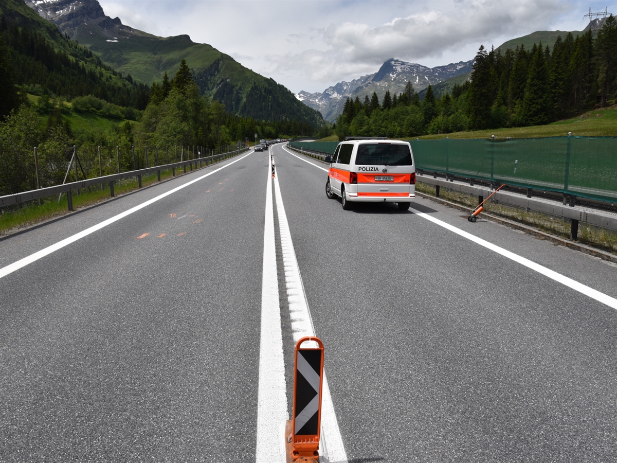 Aufnahme ab Strassenmitte bei der doppelten Sicherheitslinie und einer Leitbake. Auf der linken Fahrbahnhälfte orange markierte Kollisionsspuren. Auf der rechten Fahrbahnhälfte ein Polizeiauto.