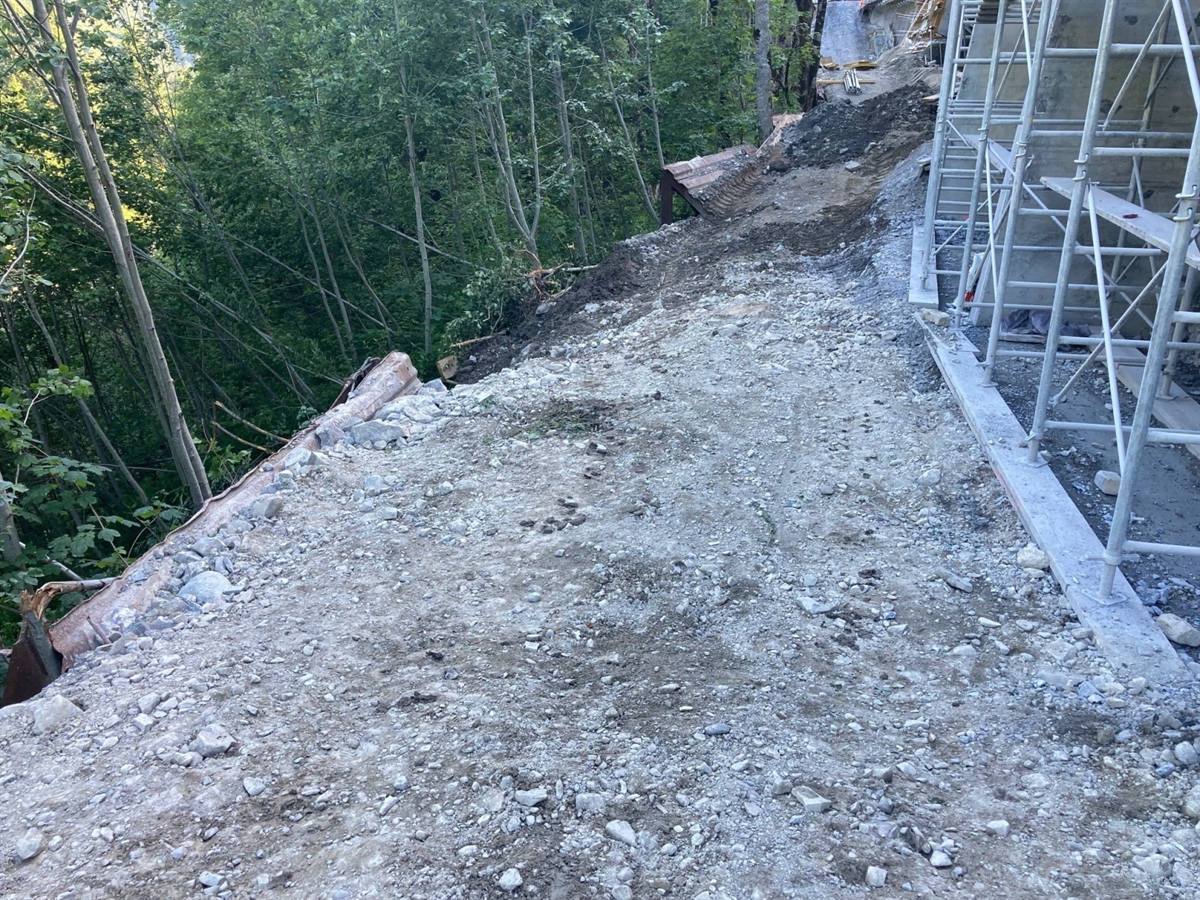 Schmaler provisorischer Baustellenweg. Rechts begrenzt ein Gerüst den Weg und links der steile Abhang