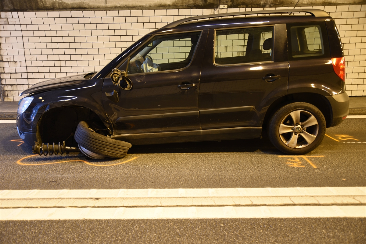 Schwarzes Auto im Seitenprofil. Linkes Vorderrad komplett ausgerissen und verdreht. Das Auto steht im Tunnel.