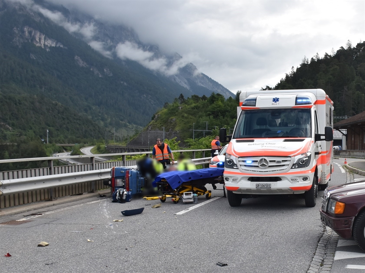 Die Verzweigung beim Bahnhof Reichenau/Tamins. Am rechten Bildrand die Front vom Auto, welches auf die Hauptstrasse einfahren wollte. In Bildmitte das auf der Seite liegende Motorrad sowie ein Ambulanzfahrzeug. Zwischen den beiden Fahrzeugen wird die verunfallte Person betreut.