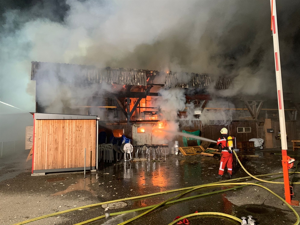 Der Holzschuppen an der Schulstrasse in Landquart. Flammen lodern im Gebäude und ein Feuerwehrmann bekämpft diese mit Löschwasser.