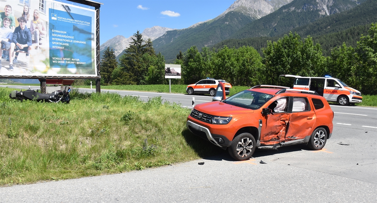 Links die Unfallstelle. Vor einer Werbetafel liegt das Motorrad. Zwei Polizeiautos am Strassenrand. Im Hintergrund Berge.
