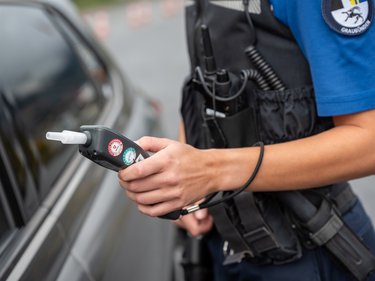 Ein Alkoholmessgerät, welches von einer Polizistin zur Fahrertüre eines Autos hingehalten wird.
